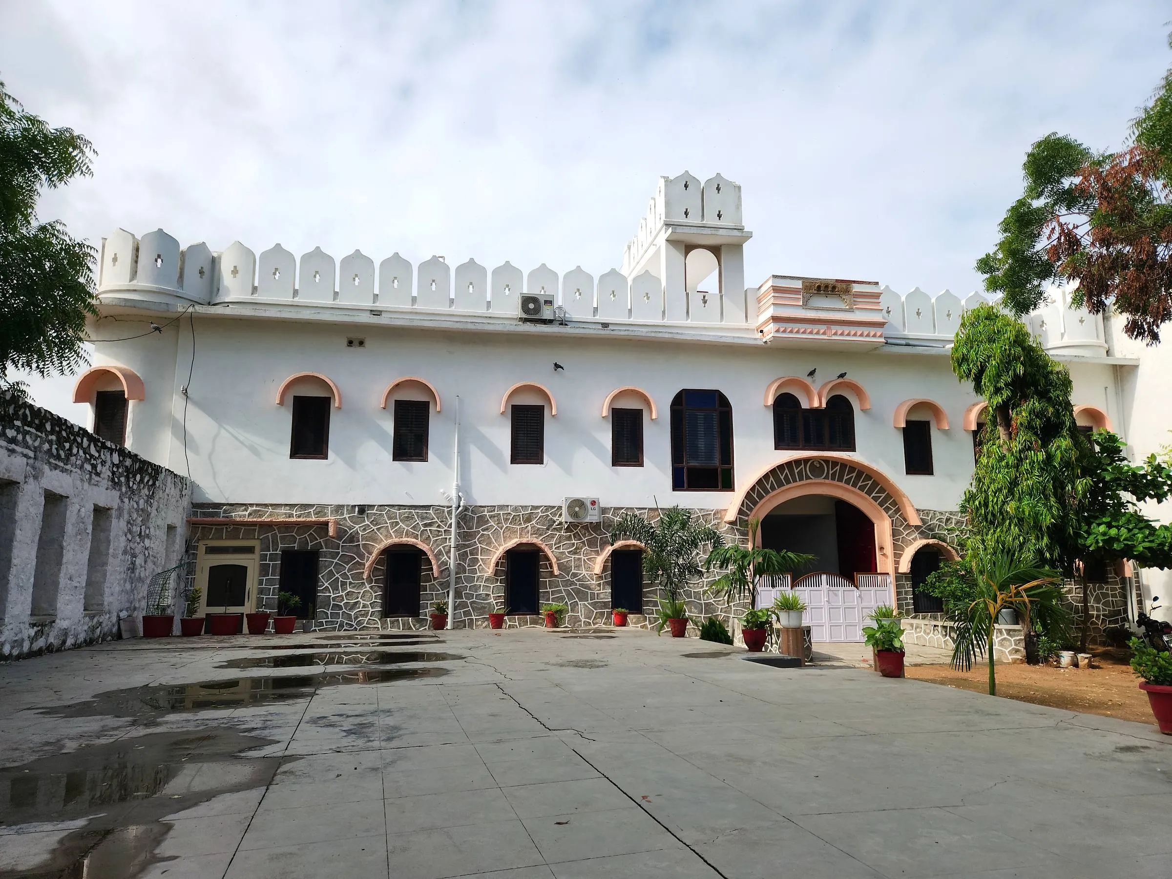 The full length of Rawla Bankli seen across its paved courtyard — two tiers of arched windows under a scalloped white parapet